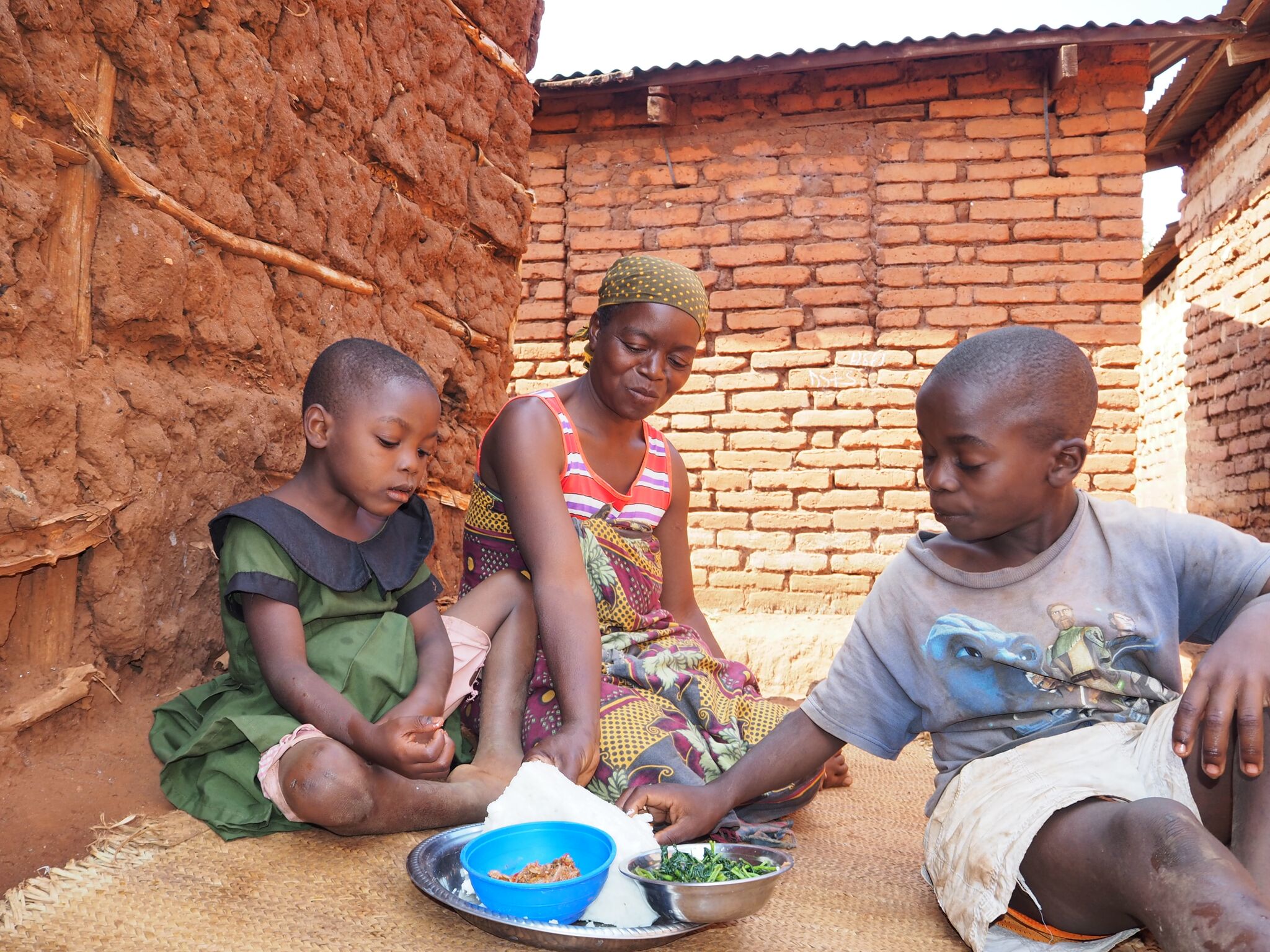 Mama Asha smirking and kids eating ugali